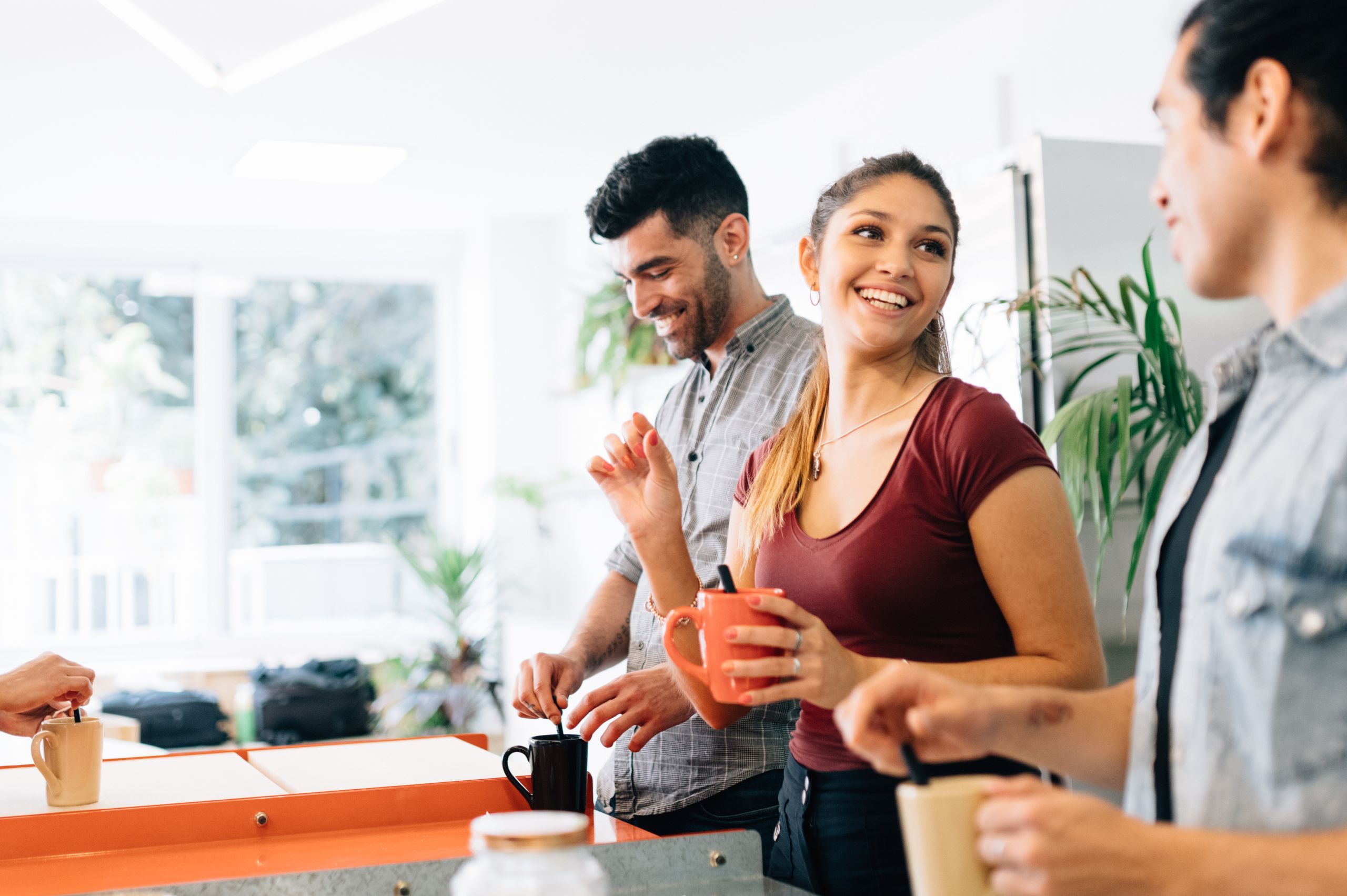 two men and a woman making coffee in a coworking space while laughing together