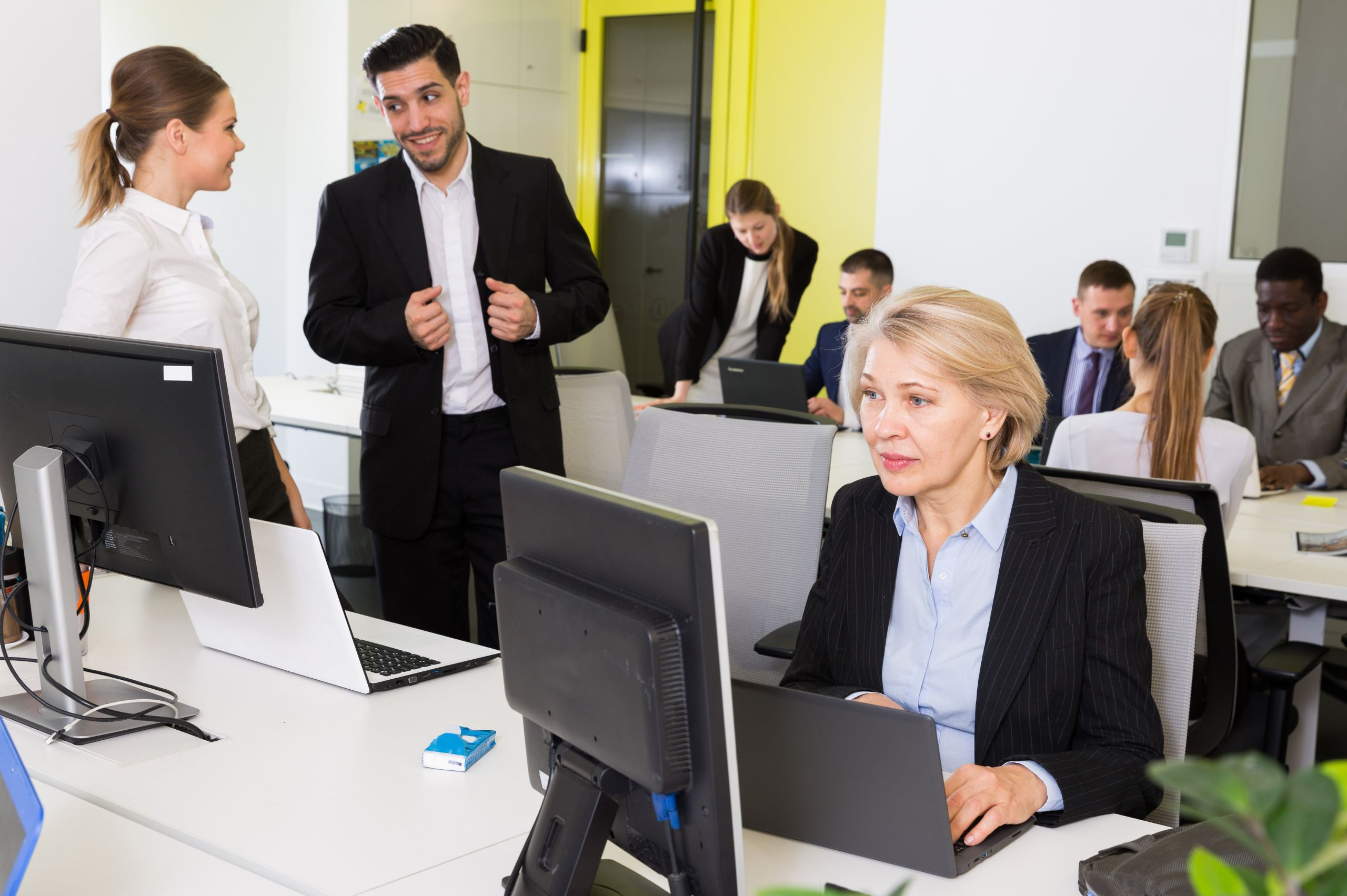 men and women working and collaborating at desks with monitors in a coworking space