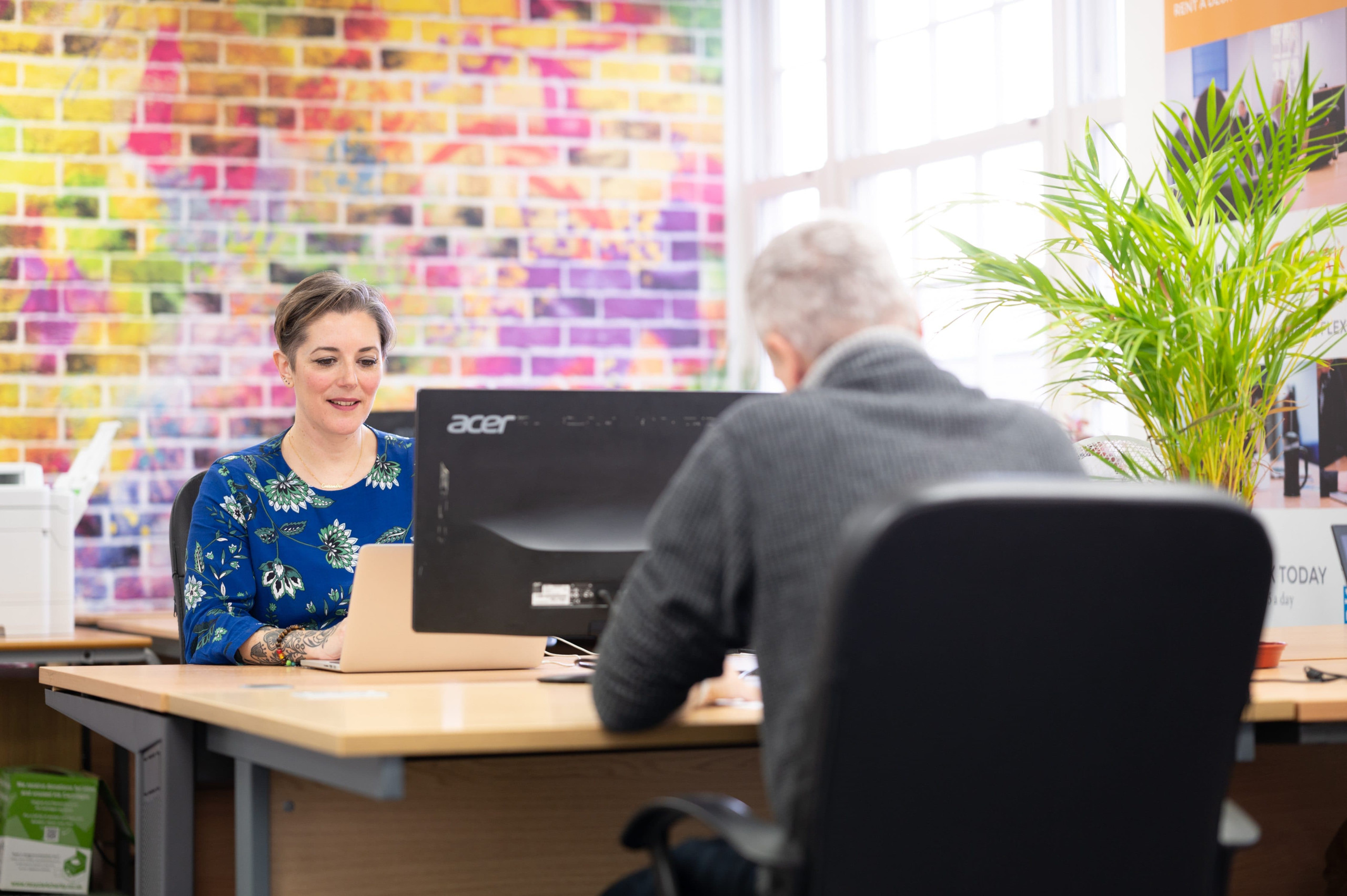 A woman sitting at an office desk with a coloured wall behind