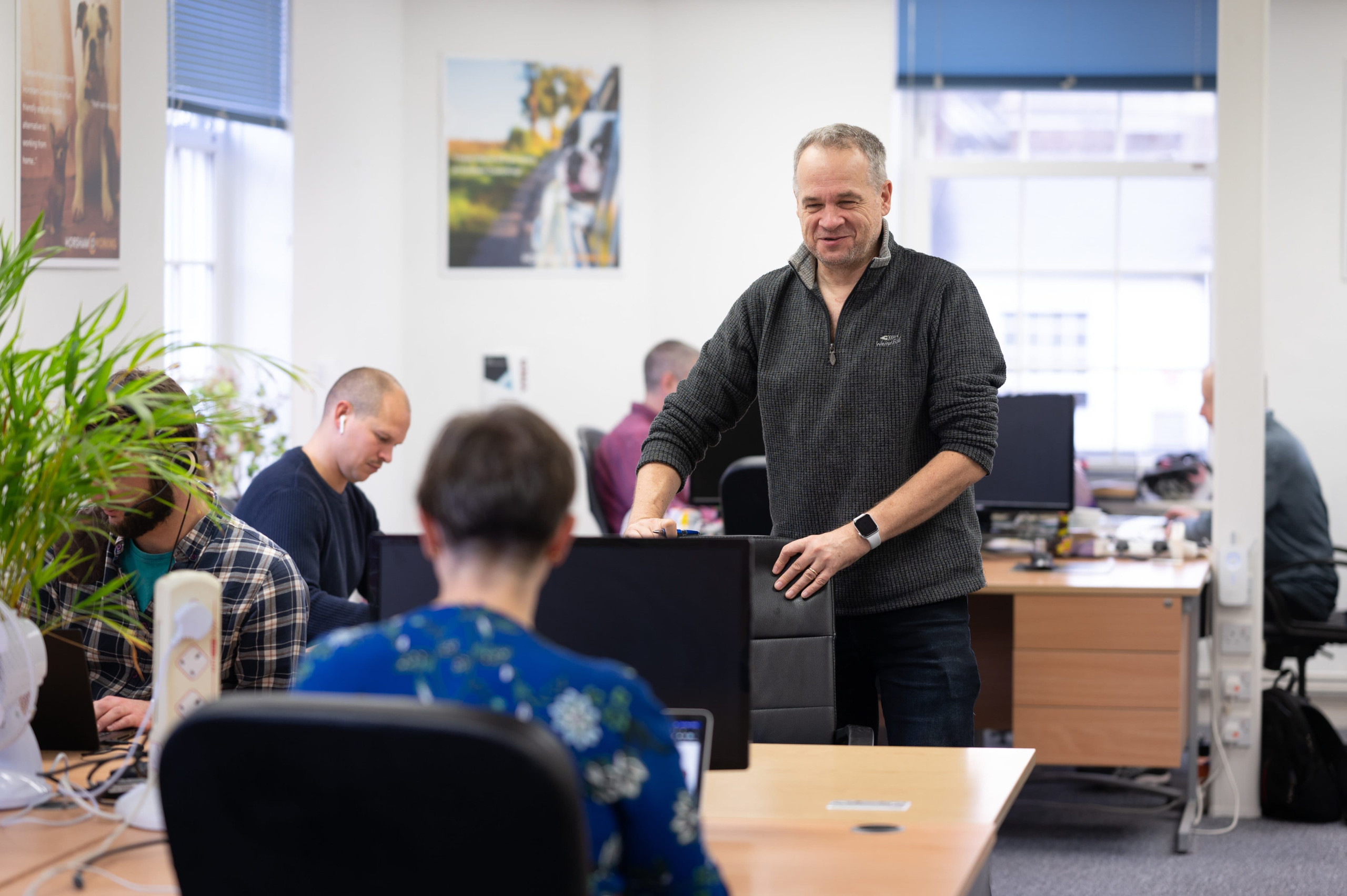 A man standing at a desk talking to other people sitting at the desk