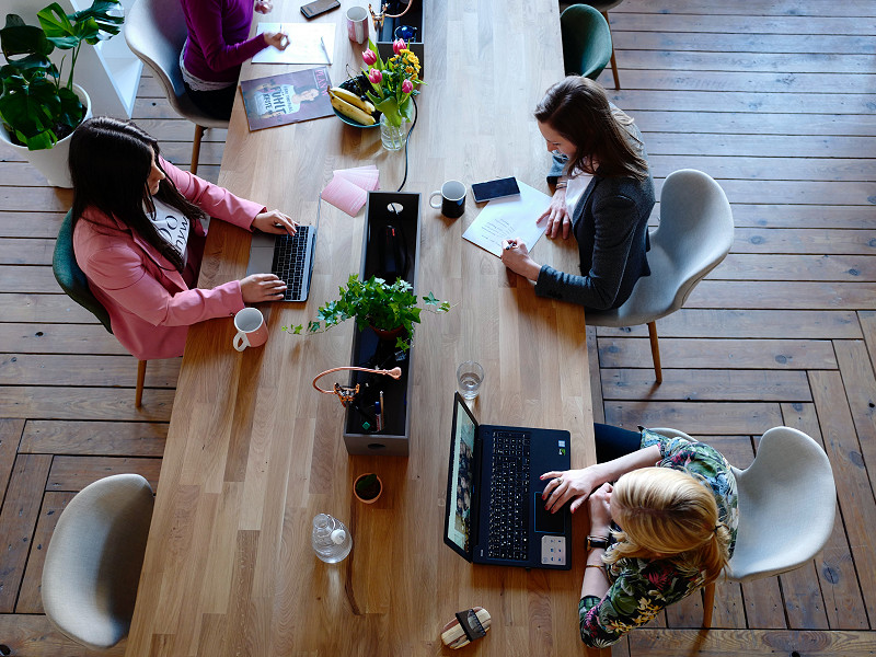 A view from above of three women with laptops at a wooden table