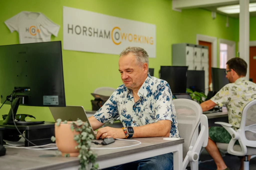 Roger working at a desk with Horsham Coworking banner behind
